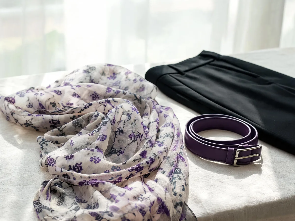 Alvin's Club — a lightweight patterned shawl arranged across a linen-covered table beside a slim belt and tailored trousers